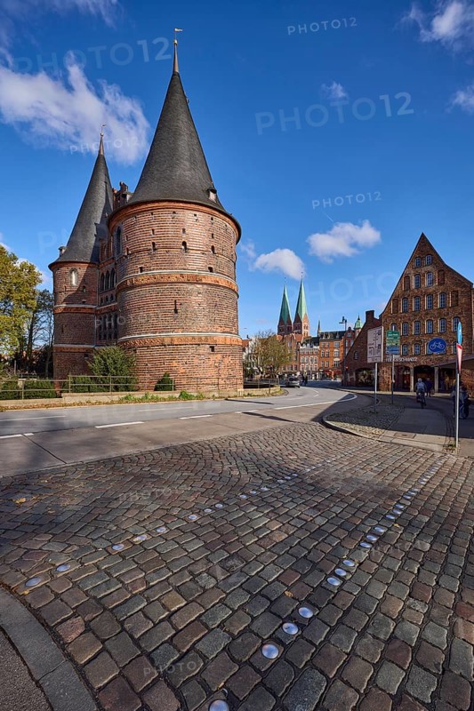 Lübeck Holstentor, side view, pedestrian crossing, cobblestone pavement, blue sky with fair weather clouds, intersection Wallstraße with Holstentorplatz, Hanseatic city of Lübeck, Schleswig-Holstein, Germany, Europe