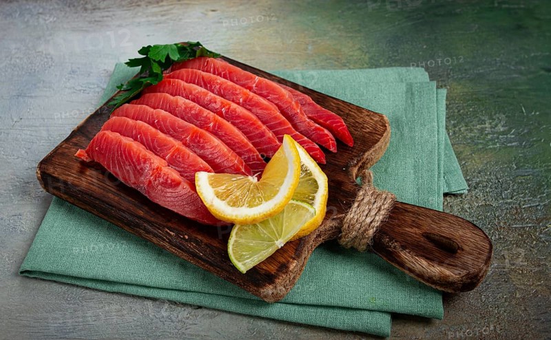 Chum salmon, cold smoked, sliced, on a cutting board, with lemon and parsley, top view, close-up, no people