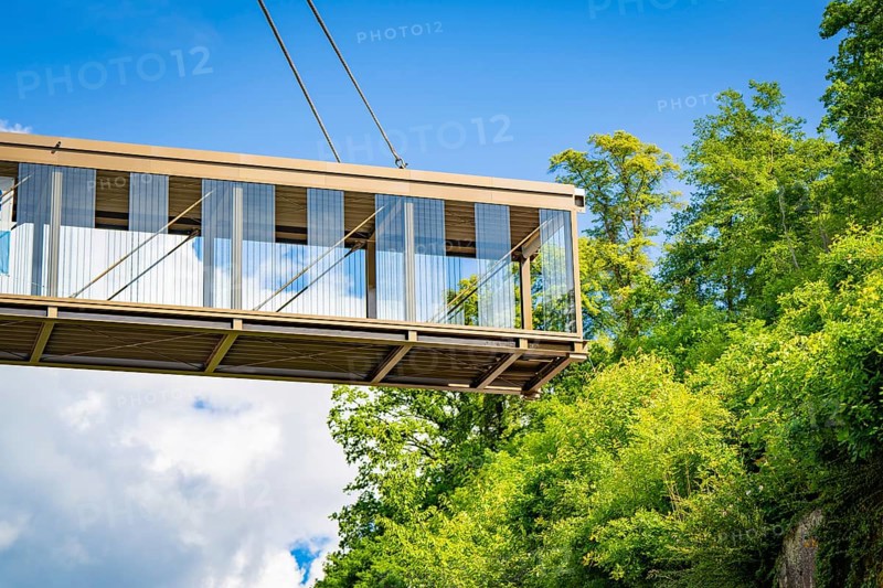 Close-up of a suspended bridge held by a crane, surrounded by green plants in sunny weather, bridge lifting Hermann Hesse railway, Calw, Germany, Europe