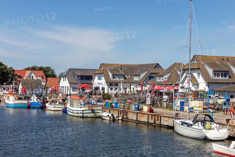 Boats at the harbour in front of small restaurants and shops under a blue sky in summer, Rügen, Hiddensee