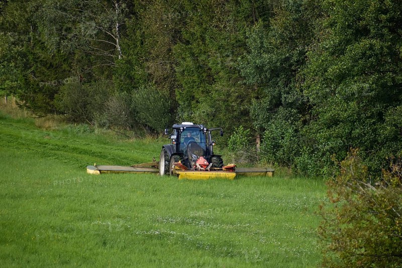 Farmer with a Valtra tractor mowing at the edge of a forest with 3 mowers at the same time, Chiemgau, Bavaria, Germany, Europe