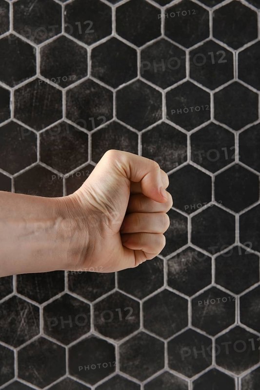 A strong fist is positioned in front of a textured hexagonal pattern, showcasing tension and strength. The visual conveys a sense of determination and focus in artistic expression