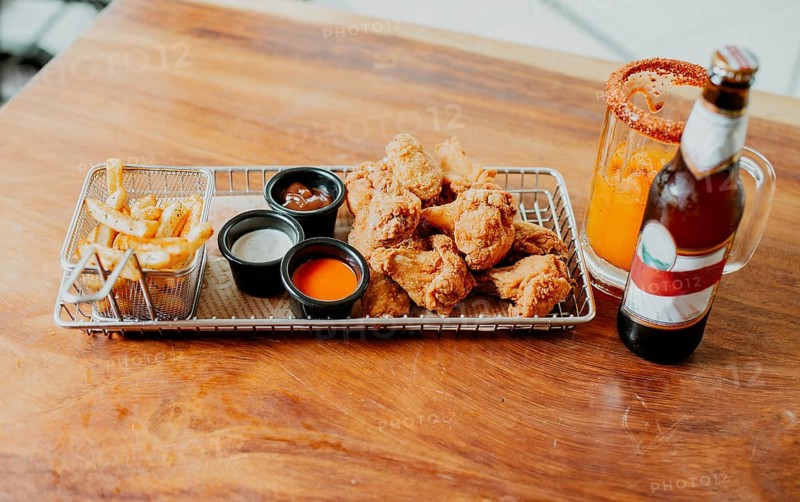 Top view of spicy wings with fries and michelada accompanied with beer served on wooden table
