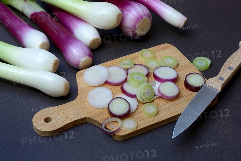 Spring onions and onion rings with a knife on a wooden board, spring onion