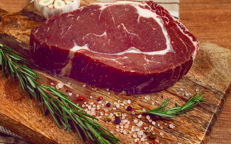 Raw steak, beef steak, rib eye steak, on a cutting board, freshly frozen, with spices and herbs, on the table, top view