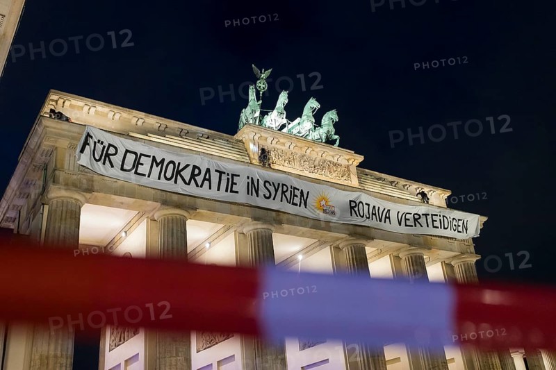 A banner For Democracy in Syria / Defend Rojava hangs behind a police barrier at the Brandenburg Tor, Berlin, 16 December 2024