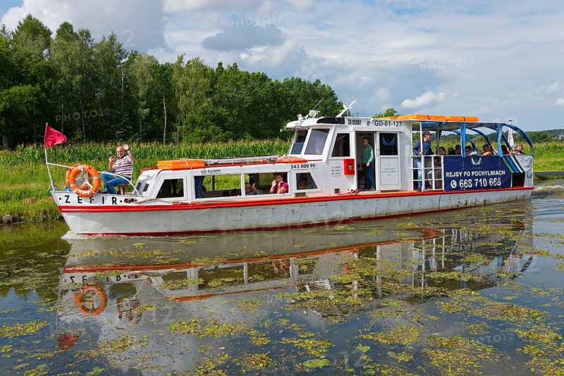 A white and red passenger boat sails along a quiet canal, surrounded by green nature, Zefir ship, Upland Canal, Warminsko-Mazurskie, Warminsko-Mazurskie, Poland, Europe