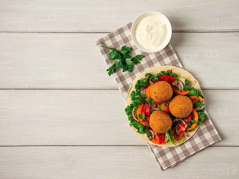 Tortillas, wrapped falafel balls, with fresh vegetables, vegetarian healthy food, on a wooden white background, no people, selective focus