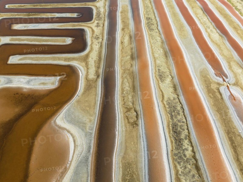 Saline ponds at the salt works near Chiclana de la Frontera. The orange-red colour depends on the level of salinity and is directly caused by the algae Dunaliella salina and brine shrimp. Aerial view. Drone shot. Cádiz province, Andalusia, Spain, Europe