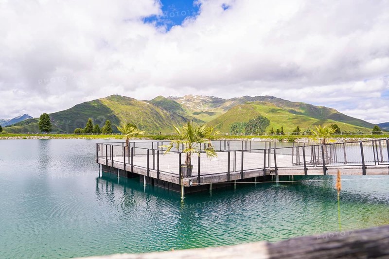 A tranquil lake with a pier, surrounded by a beautiful hilly and mountain landscape under a partly cloudy sky, Penken, Zillertal, Austria, Europe