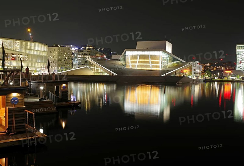 Illuminated opera house and modern buildings reflected in calm waters at night, Oslo city centre, Norway, Europe