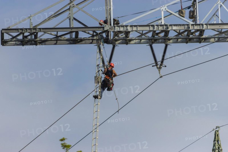 A technician works on a high-voltage pylon under a clear blue sky
