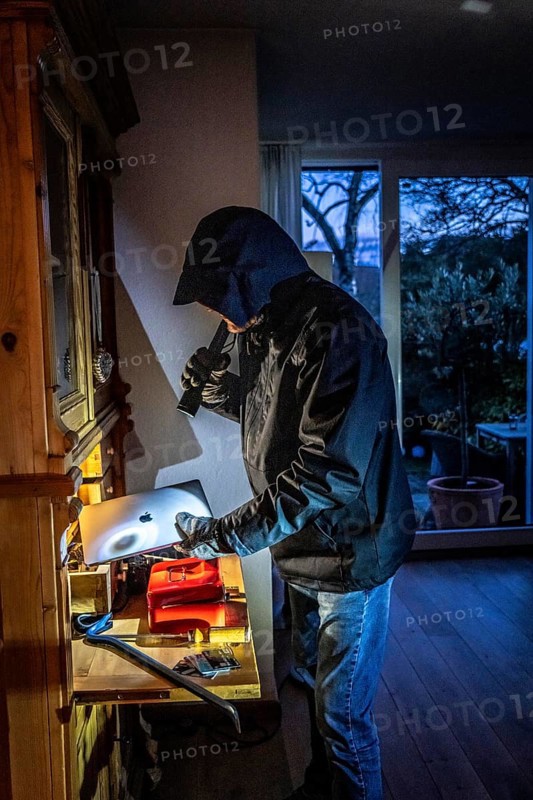 Symbolic image of a burglary, perpetrator has broken into a flat from the garden side and is looking for loot, computer, laptop, valuables, money, technology