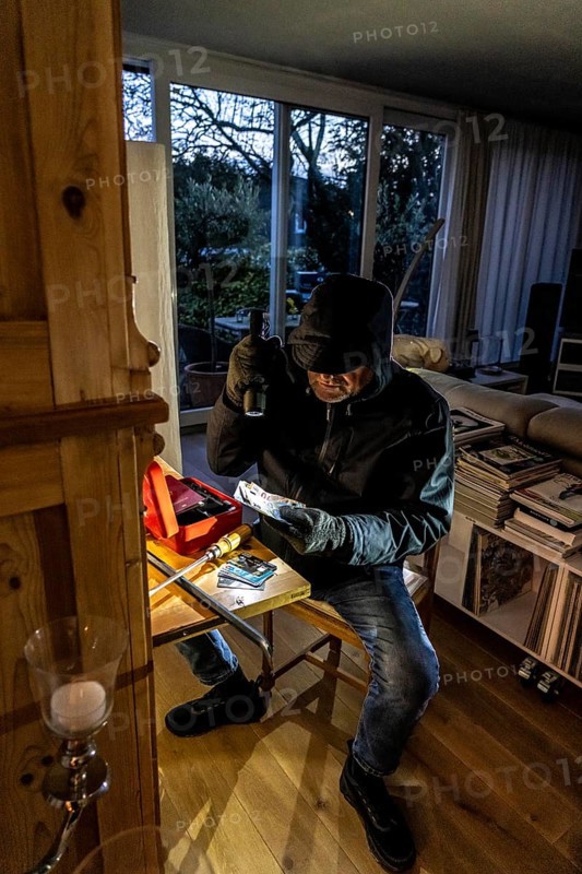 Symbolic image of a burglary, perpetrator has broken into a flat from the garden side and is looking for loot, breaks open a cash box, finds valuables, money