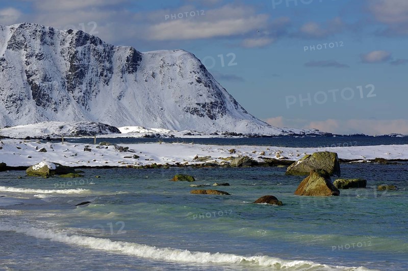 Snowy beach with rocky mountains in the background, gentle waves in the blue sea, calm winter atmosphere, Ramberg, Flakstad, Lofoten, Nordland, Norway, Europe