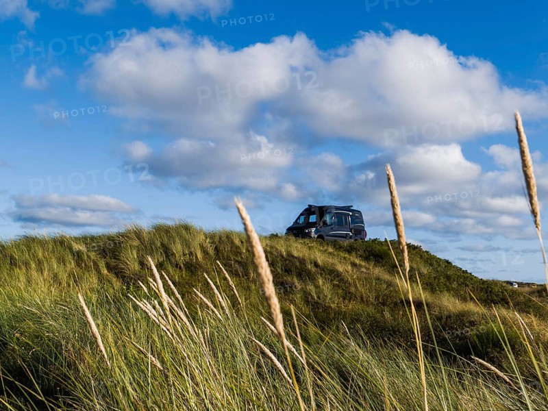 A campervan stands on a grassy dune under a blue sky with clouds, North Sea, Jutland, Denmark, Europe