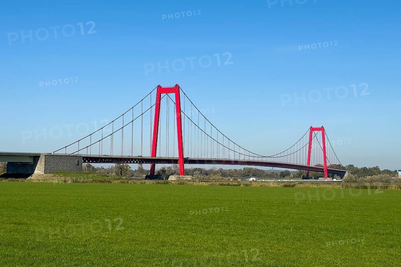 View over Rhine meadows on the left bank of the Rhine to red steel pillars of earth-anchored suspension bridge nicknamed Golden Gate of the Lower Rhine, 1228 metres in total length, longest suspension bridge in Germany, Emmerich, North Rhine-Westphalia, Germany, Europe