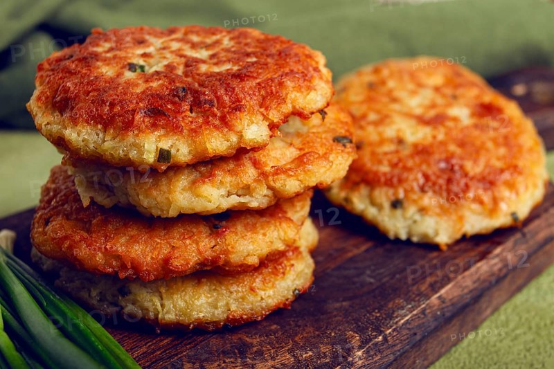 Crispy potato pancakes Latkes, stacked on a wooden board next to fresh green onions, natural light, homemade, no people