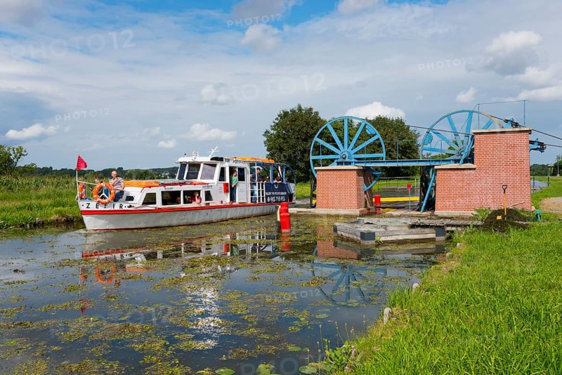 A boat passes a lock in a green landscape in sunny weather, ship Zefir, manoeuvrable wheels in the lower pillar for aligning the rope for the rail cars, Upland Canal, Warminsko-Mazurskie, Poland, Europe