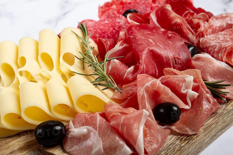 Assorted meat, appetizer, prosciutto, salami and ham, with maasdam cheese and olives, on a wooden board, breakfast, top view, close-up, no people