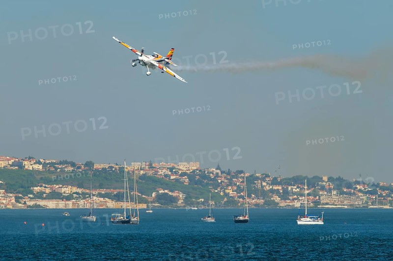Stunt aerobatic plane Edge 540 performing stunts in blue sky at Oeiras Air Show above yacht boats