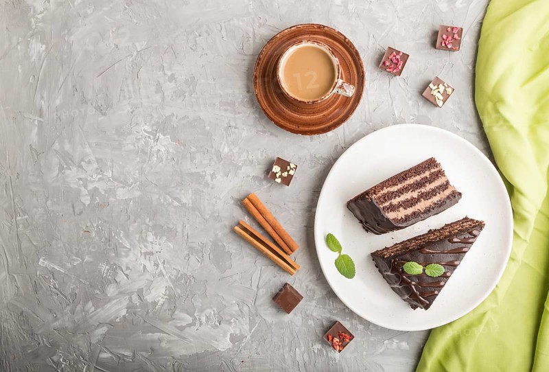 Homemade chocolate cake with milk cream and a cup of coffee on a gray concrete background with green textile. top view, flat lay, copy space