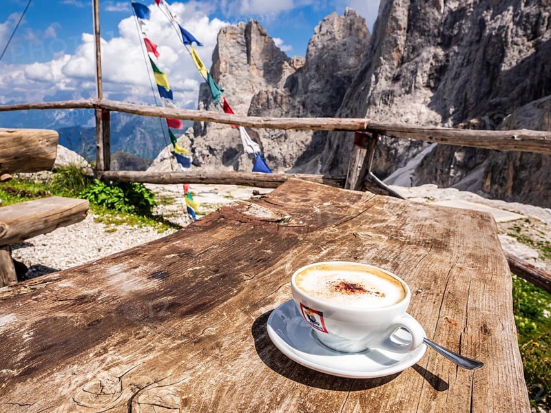 A cup of cappuccino, tibetian flag of prayer, mountain hut Rifugio Mulaz, Pala mountain group in the back, dolomites, Trentino, Italy, Europe