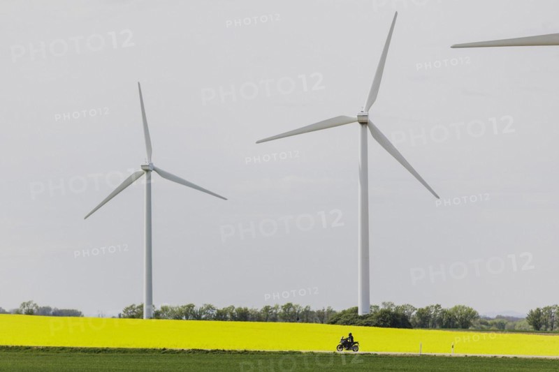 A motorbike on a country road stands out in front of a rapeseed field and wind turbines in Vierkirchen, 12.04.2024