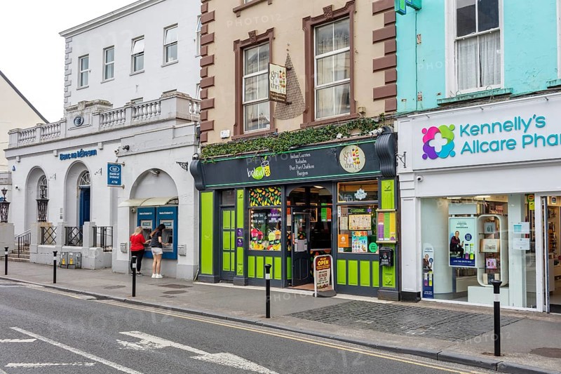 Shops and pharmacy along a busy street with mixed historic and modern facades, Tralee