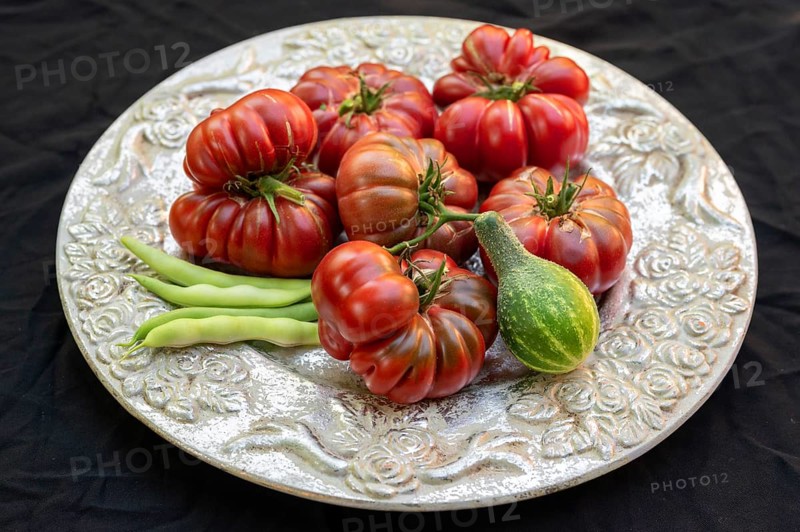 Tomatoes, ox hearts and a Vorgebirgstrauben pickled cucumber on a decorative plate on a black background, Baden-Württemberg, Germany, Europe