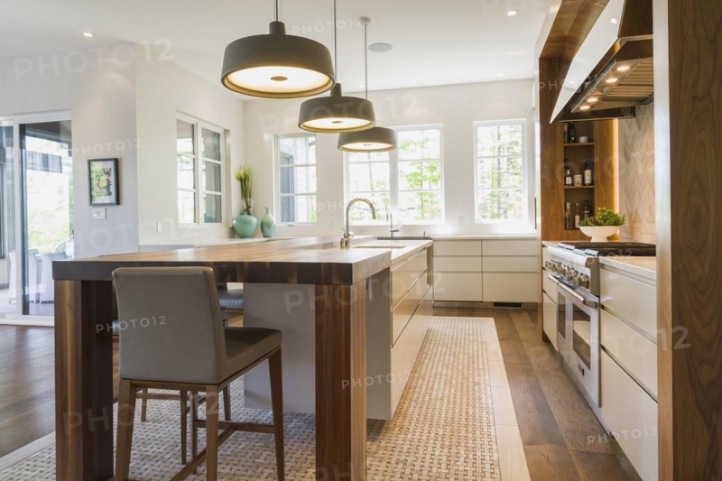 Walnut wood island with grey leather and wooden high chairs on travertine mosaic floor surrounded by engineered hickory wood floorboards in kitchen inside a luxurious contemporary bungalow style home, Quebec, Canada, North America