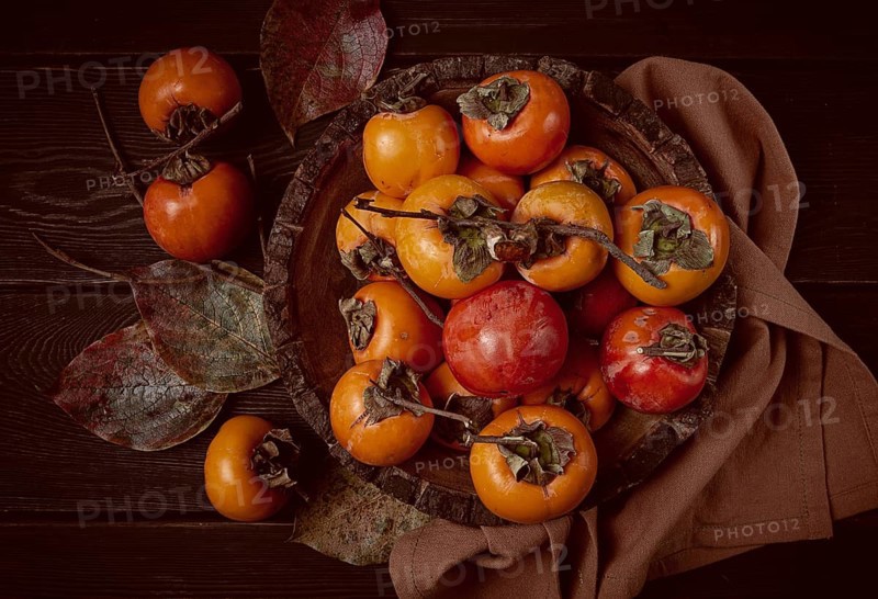 Fresh persimmon, in a wooden plate, top view, no people