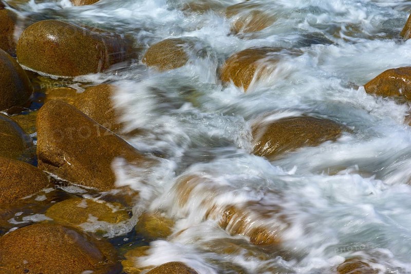 Water flows over brown stones surrounded by waves. Dynamic and natural atmosphere, Point du Millier, Beuzec Cap Sizun, Finistere, Brittany, France, Europe