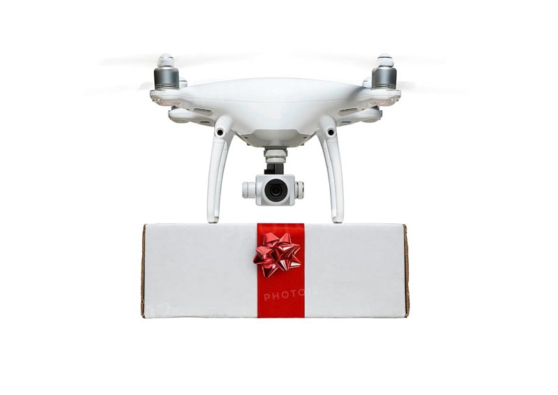 Unmanned UAV drone quadcopter delivering A package with a red ribbon and bow isolated on a white background.