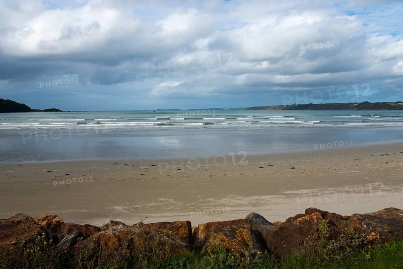 Lonely beach with gentle waves, covered by a cloudy sky and surrounded by rocks, Plage Saint Efflamm, Plestin-les-Grèves, Breton Plistin, Arrondissement Lannion, Côtes-d'Armor, Brittany, France, Europe