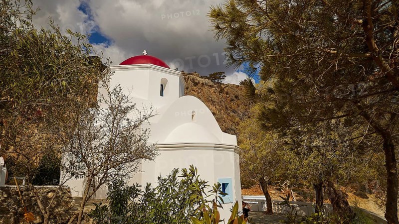 A picturesque white church with a red dome, surrounded by trees and rocks under a changeable sky, Kyra Panagia, Kyra Panagia Beach, East Coast, Karpathos, Dodecanese, Greek Islands, Greece, Europe