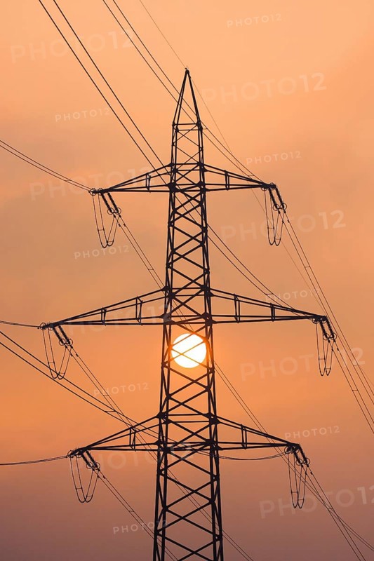 Setting sun behind silhouette of high-voltage power line pylons, shrouded in orange light amidst fog, Canton Zurich, Switzerland, Europe