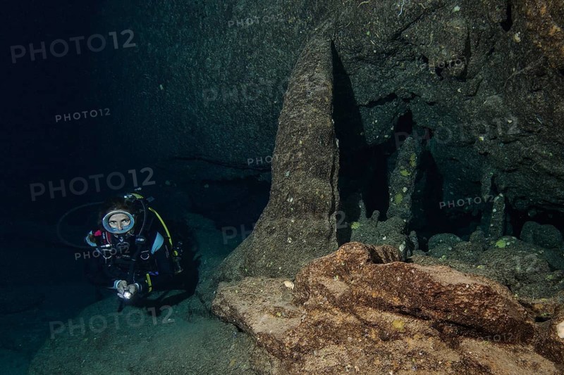 Diver swims diving through underwater cave with stalactites weathered by salt water in marine reserve Reserva Marina de Llevant, Mediterranean Sea, Balearic Islands, Cala Ratjada, Majorca, Spain, Europe