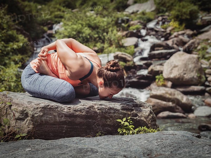 Vintage retro effect filtered hipster style image of Young sporty fit woman doing yoga, meditating in Baddha Padmasana (Bound Lotus Pose) outdoors at tropical waterfall