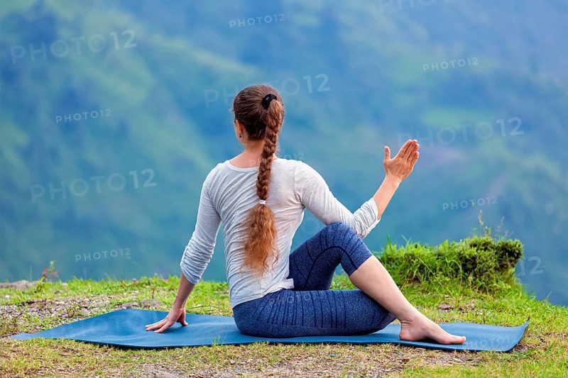 Hatha yoga outdoors, sporty fit woman doing yoga asana Parivrtta Marichyasana (or ardha matsyendrasana), seated spinal twist outdoors in mountains
