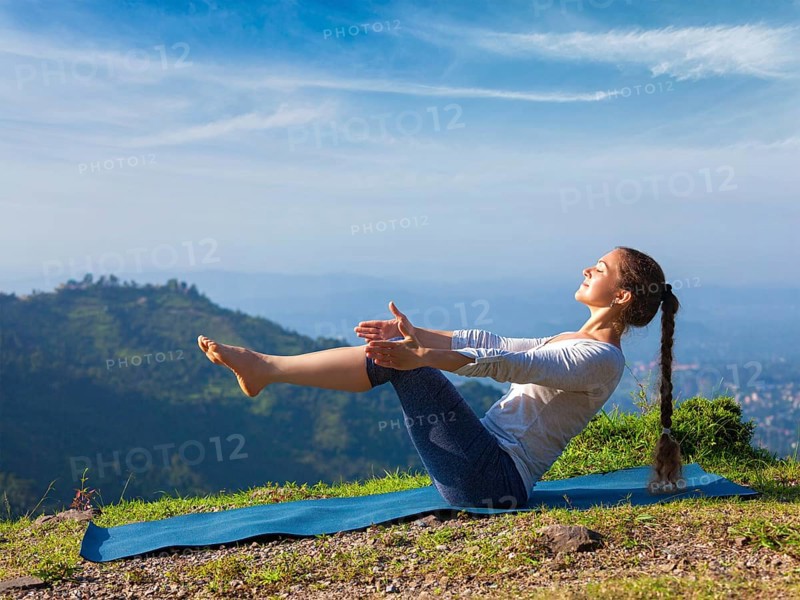 Yoga outdoors, young sporty fit woman doing Ashtanga Vinyasa Yoga asana Navasana, boat pose easy beginner variation, in Himalayas mountains in the morning Himachal Pradesh, India, Asia