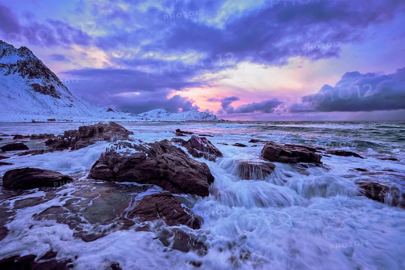 Waves of Norwegian sea on rocky coast in fjord on sunset with sun. Skagsanden beach, Lofoten islands, Norway, Europe