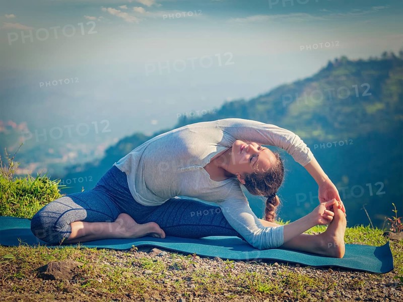 Yoga outdoors, young sporty fit woman doing Hatha Yoga asana parivritta janu sirsasana, Revolved Head-to-Knee Pose, in mountains in the morning. Vintage retro effect filtered hipster style image