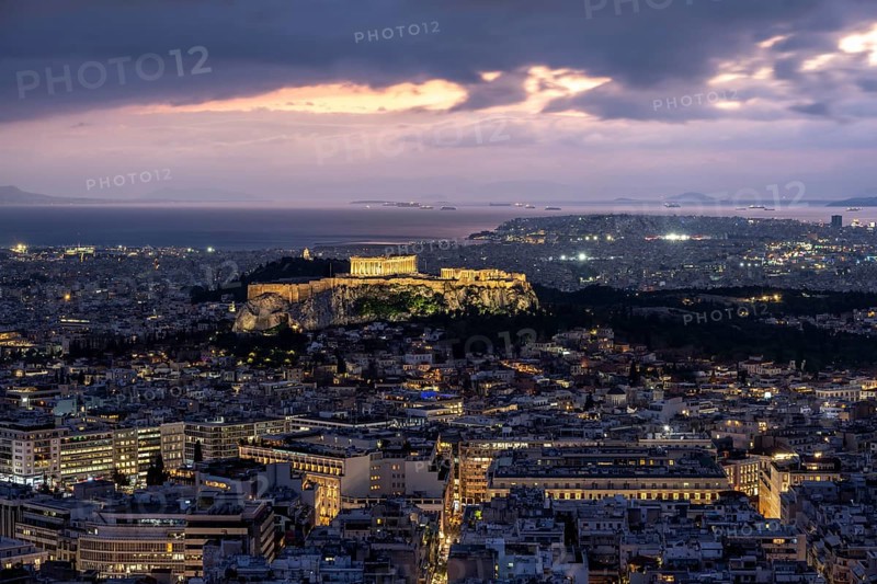 View over the sea of houses of Athens, illuminated Parthenon temple on the Acropolis, dramatic cloudy sky at sunset, from Mount Lycabettus, Athens, Greece, Europe