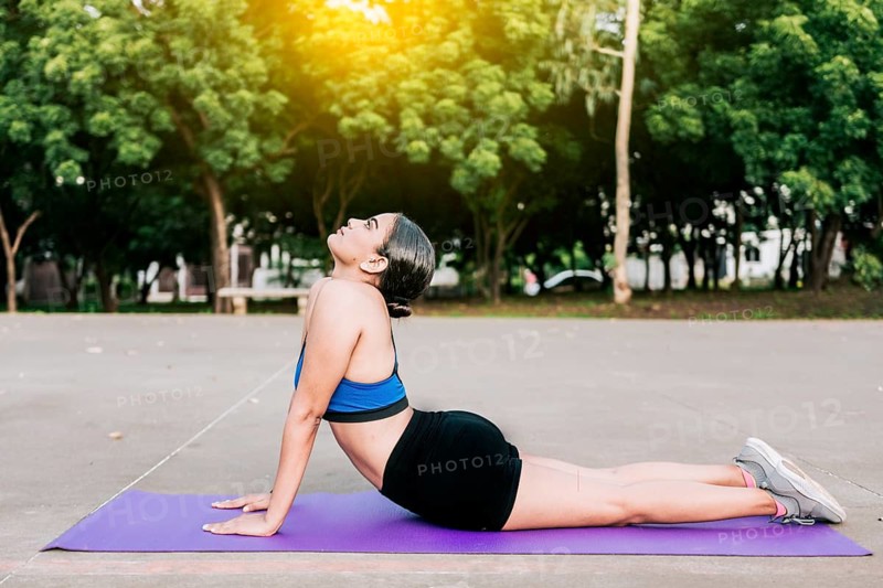 Sporty woman stretching her body doing cobra pose in a park. Athlete woman doing cobra pose in a park. Athlete woman doing yoga Bhujangasana in a park, Managua, Nicaragua, Central America