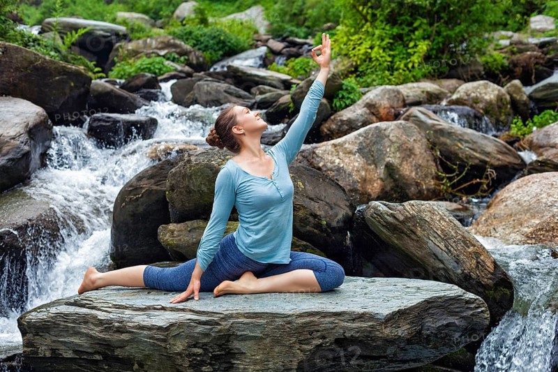 Yoga outdoors, young sporty fit woman doing stretching yoga asana Eka pada rajakapotasana, one-legged king pigeon pose at tropical waterfall