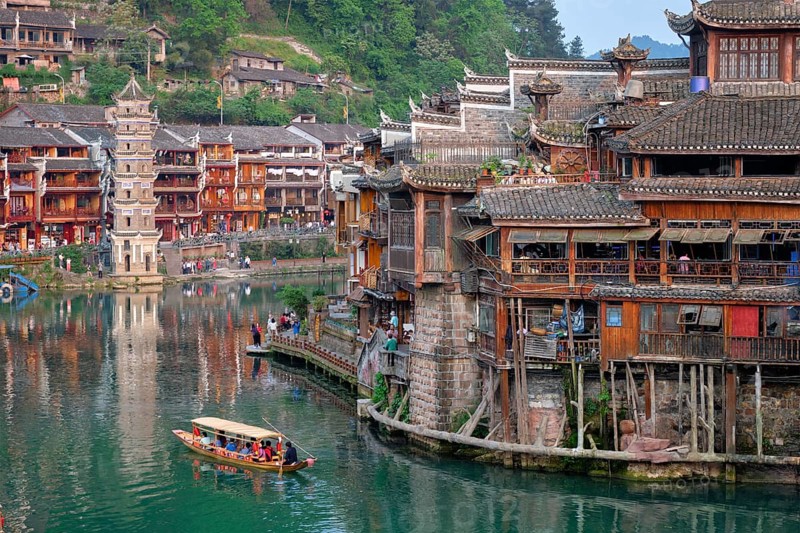 Chinese tourist attraction destination, Feng Huang Ancient Town (Phoenix Ancient Town) on Tuo Jiang River with Wanming Pagoda tower and tourist boat. Hunan Province, China, Asia