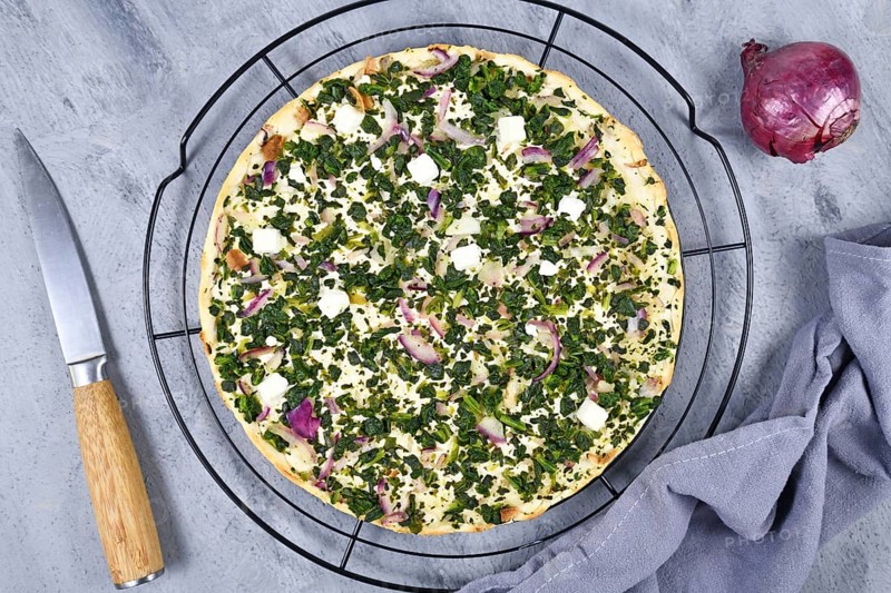 Flammkuche or Tarte Flambee, a thin pizza-like baked pie from German-French Alsace border region, vegetarian variation with spinach, red onions and feta cheese