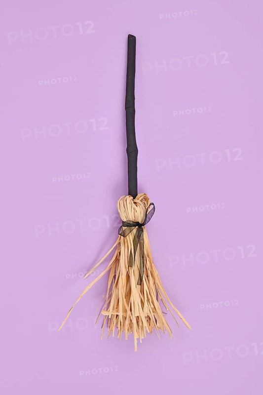 Witch broom with black twig and straw bristles on violet background