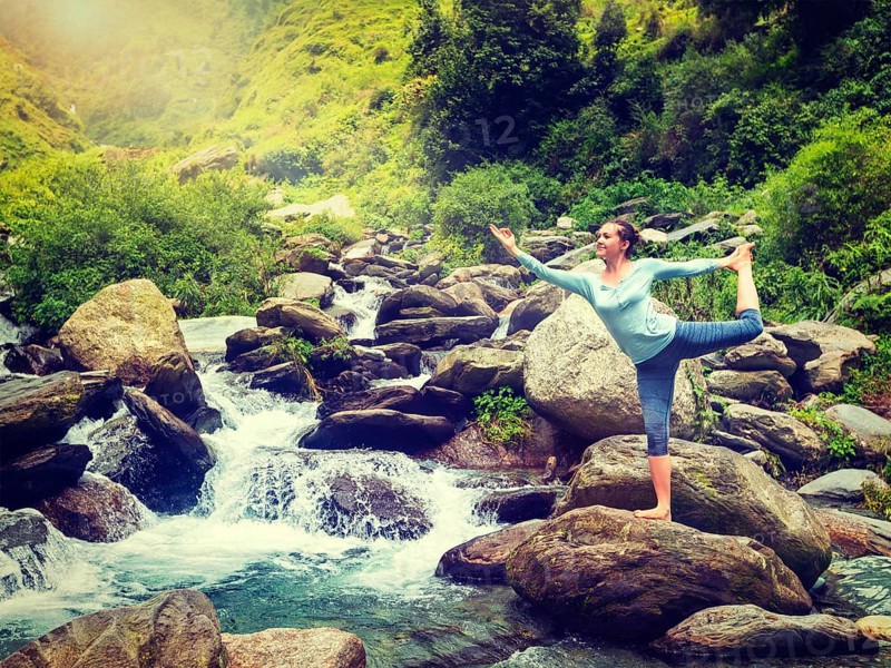 Yoga outdoors, woman doing yoga asana Natarajasana, Lord of the dance balance pose outdoors at waterfall in Himalayas. Vintage retro effect filtered hipster style image